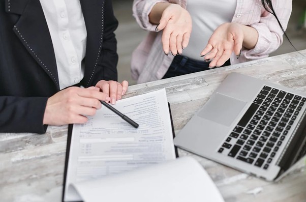 Two people sitting at a desk with a laptop and forms.